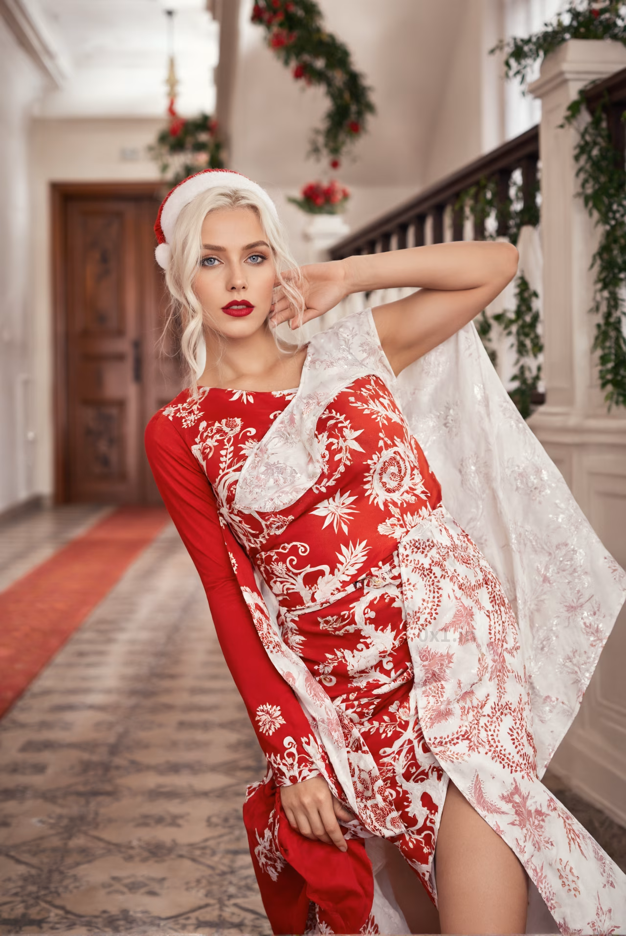 Close-up of a 24-year-old Belgian woman wearing a red and white cocktail dress and a Santa Claus hat in a Christmas decorated hallway.