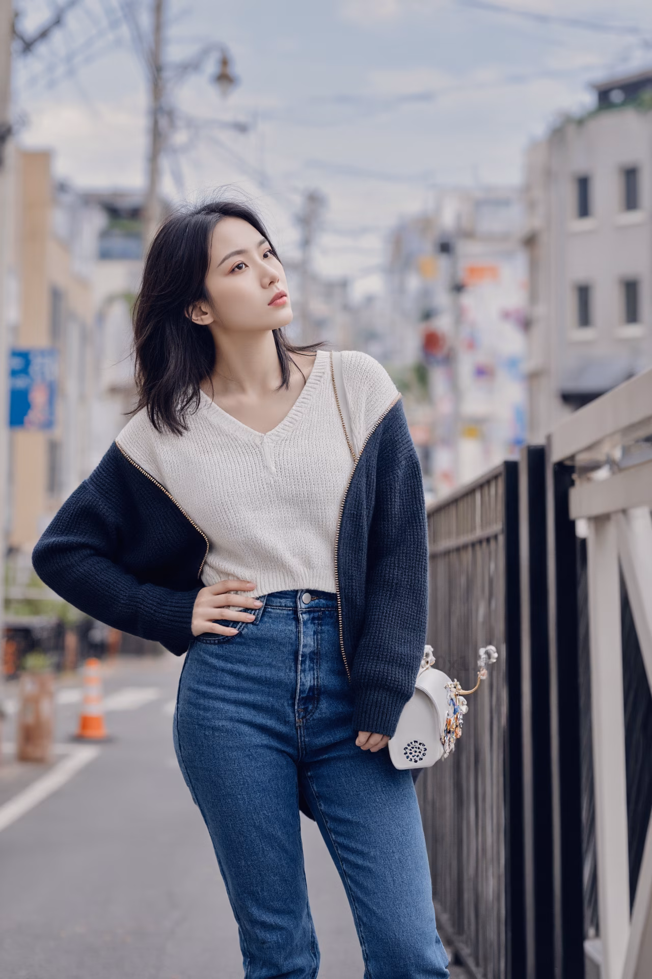 Close-up portrait of a slim Japanese woman wearing an oversized hoodie and bootcut jeans, surrounded by a Japanese street backdrop.