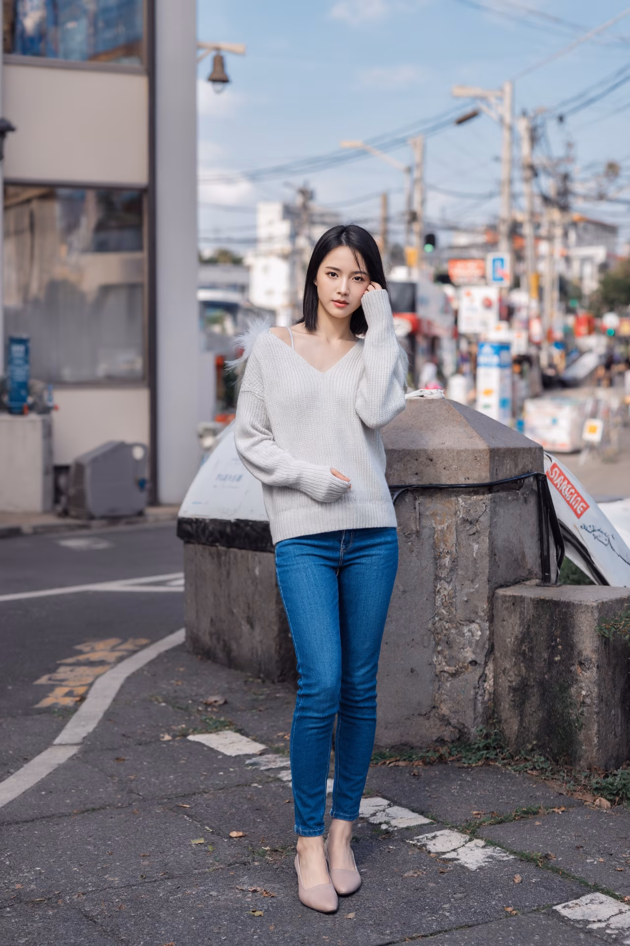 Close-up portrait of a slim Japanese woman wearing an oversized hoodie and bootcut jeans, surrounded by a Japanese street backdrop.