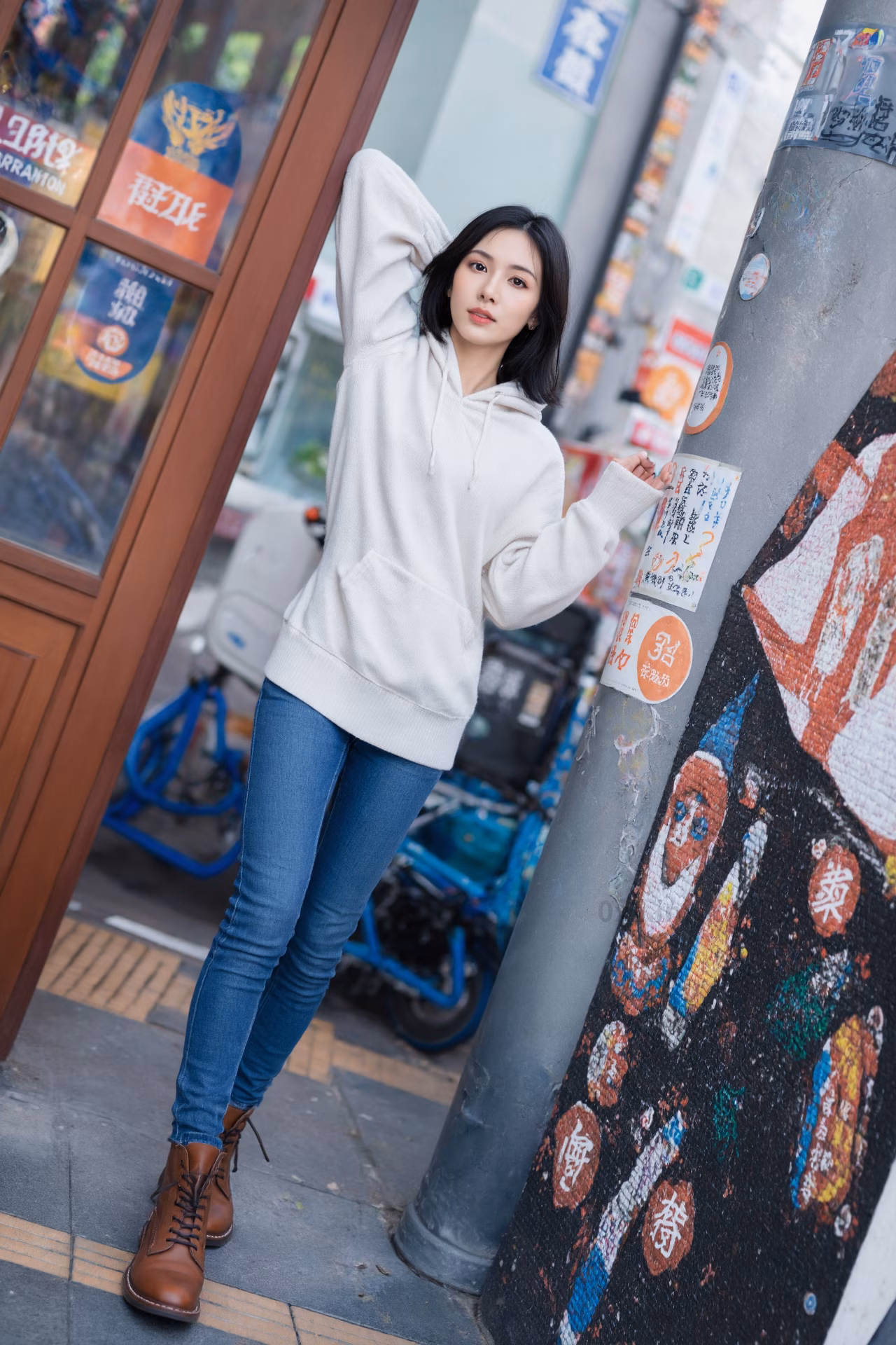 Close-up portrait of a slim Japanese woman wearing an oversized hoodie and bootcut jeans, surrounded by a Japanese street backdrop.