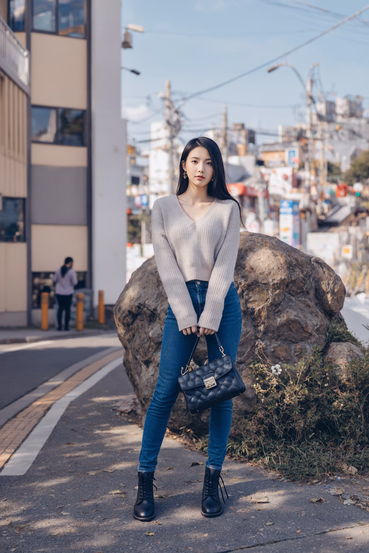 Close-up portrait of a slim Japanese woman wearing an oversized hoodie and bootcut jeans, surrounded by a Japanese street backdrop.
